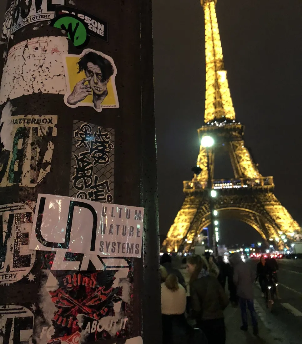 A UNS sticker on a street pole with the Eiffel Tower lit up at night