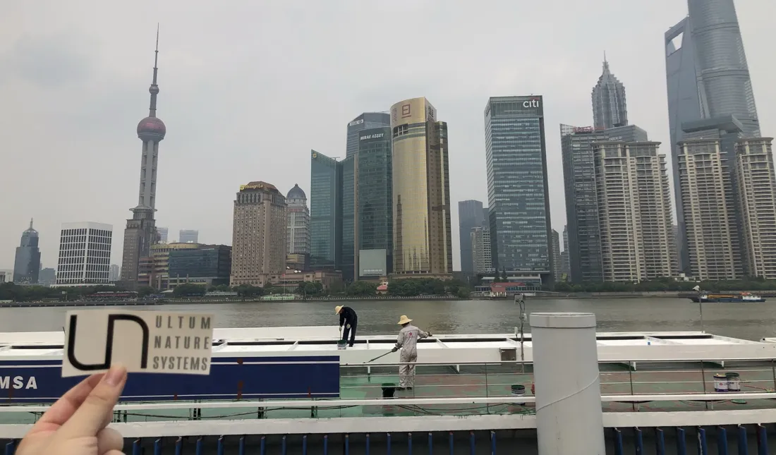 A UNS sticker held up in front of the Shanghai skyline from the Bund
